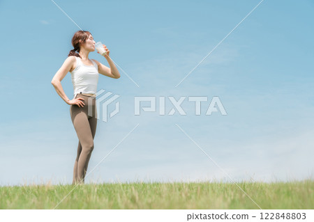 Woman drinking protein/EAA drink during exercise (blue sky) Woman drinking protein/EAA drink during exercise (blue sky) 122848803