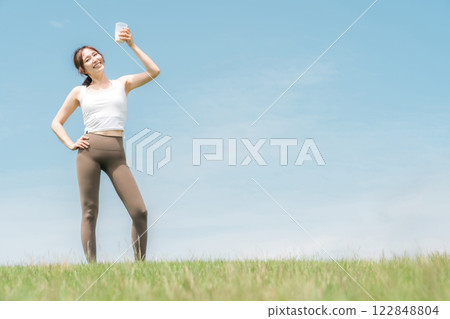 Woman drinking protein/EAA drink during exercise (blue sky) Woman drinking protein/EAA drink during exercise (blue sky) 122848804