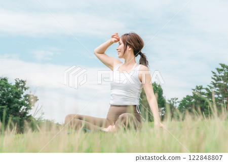 A woman meditating, doing yoga, stretching and pilates in the grassland (healthcare and diet) 122848807