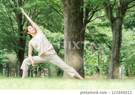 年輕的亞洲女性在公園做瑜珈、瑜珈、皮拉提斯、在森林/公園伸展運動（三角姿勢） 122848812