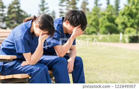 護士、護理人員和醫務人員等男女工作人員穿著工作服坐在公園的長椅上，心情低落 122849307