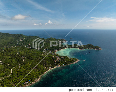 Coastal village with lush hills and a turquoise bay under a bright blue sky, showcasing serene natural beauty. Koh Tao, Thailand. Coastal village with lush hills and a turquoise bay under a bright blue sky, showcasing serene natural beauty. Koh Tao, Thailand. 122849545