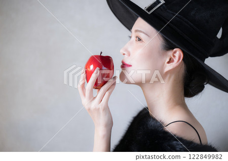 Cute villain or witch image, Halloween or cosplay profile, eating an apple Cute villain or witch image, Halloween or cosplay profile, eating an apple 122849982