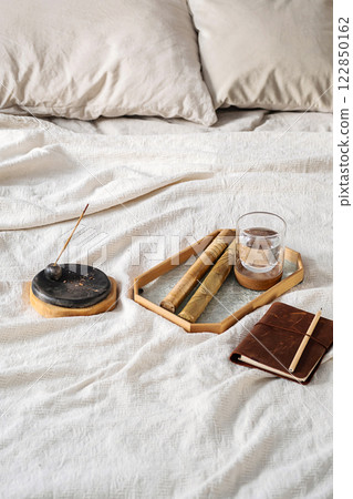 Incense Stick with Smoke, Glass of Water and Notebook on Bed. Morning Ritual Scene. Incense Stick with Smoke, Glass of Water and Notebook on Bed. Morning Ritual Scene. 122850162