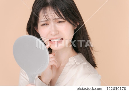 一個二十多歲的女人，一臉苦惱地看著鏡子 122850178