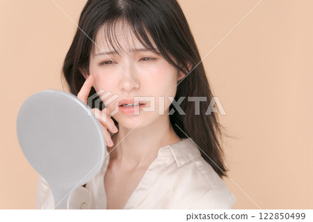 A woman in her twenties with a troubled expression looking in the mirror A woman in her twenties with a troubled expression looking in the mirror 122850499