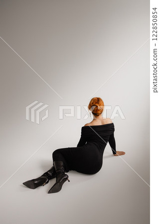 Elegant red hear woman in black dress lying on white background. Back view. Elegant red hear woman in black dress lying on white background. Back view. 122850854