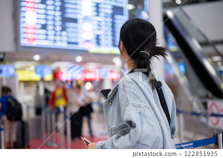 A back view of an Asian female passenger looking at a flight information display in the airport. A back view of an Asian female passenger looking at a flight information display in the airport. 122851935