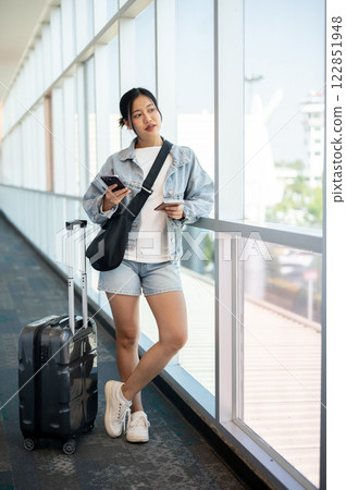 A confident Asian woman gazing at the airport runway while waiting for her flight. A confident Asian woman gazing at the airport runway while waiting for her flight. 122851948