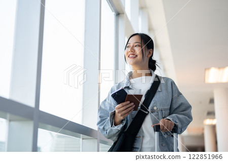 A happy Asian woman gazes out the window while standing in the airport corridor. 122851966