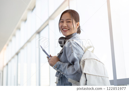A beautiful Asian female traveler, smiling at the camera while walking through the airport corridor. A beautiful Asian female traveler, smiling at the camera while walking through the airport corridor. 122851977
