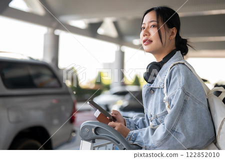 A positive Asian female traveler stands at the airport taxi pickup point, looking for her taxi. 122852010