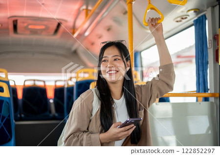 An attractive Asian woman holds a handrail while admiring the city view during her bus ride. 122852297