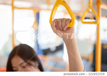 A close-up of a woman holding a handrail while commuting on a public bus in the city. 122852319