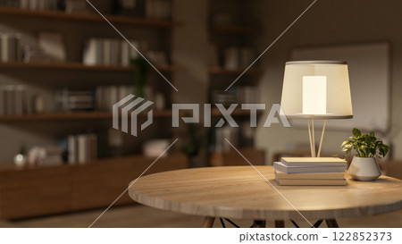 A round hardwood table with books, a decorative plant, and a table lamp in a cozy room. A round hardwood table with books, a decorative plant, and a table lamp in a cozy room. 122852373