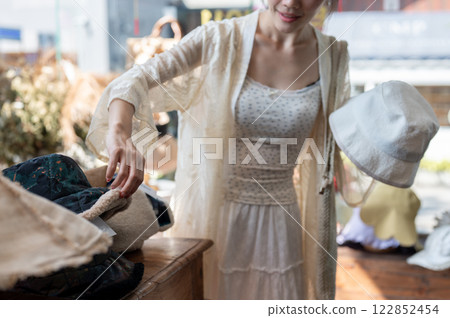 A close-up of an Asian woman carefully selecting items in a hat shop, enjoying her shopping spree. A close-up of an Asian woman carefully selecting items in a hat shop, enjoying her shopping spree. 122852454