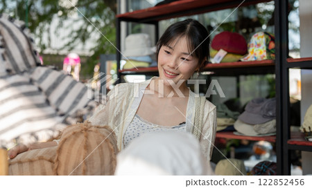 A pretty and satisfied Asian female customer enjoys selecting items to buy in a hat shop. 122852456