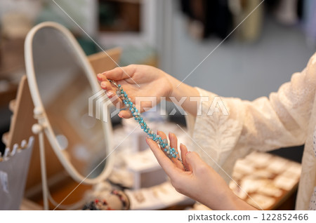 A close-up of a female customer holding a bracelet, selecting items to buy in a fashion shop. 122852466