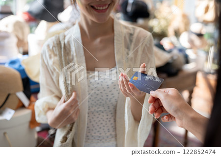 A satisfied Asian female customer handing her credit card to a shop cashier to pay for her items. A satisfied Asian female customer handing her credit card to a shop cashier to pay for her items. 122852474