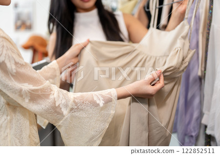 A female customer gently touching the fabric of a dress while selecting items in a clothing store. A female customer gently touching the fabric of a dress while selecting items in a clothing store. 122852511