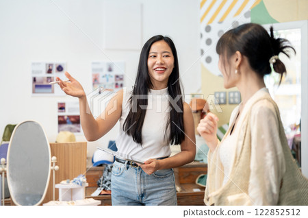 A service-minded Asian female clothing store owner is talking to a customer, working in her shop. 122852512