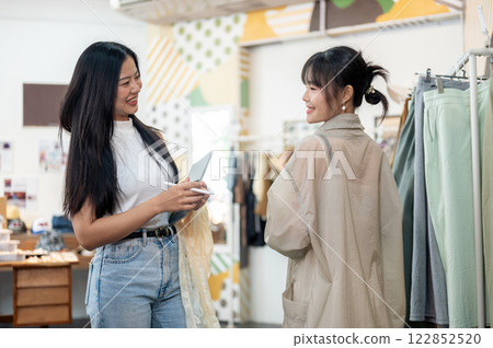 A service-minded and friendly female clothing store employee is helping a customer select an item. 122852520
