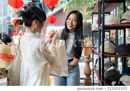 A beautiful Asian female clothing shop cashier is handing shopping bags to a customer after checkout 122852535