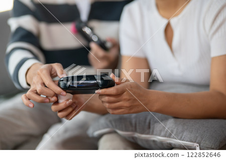 A close-up of two friends play a video game with joysticks on the sofa. 122852646