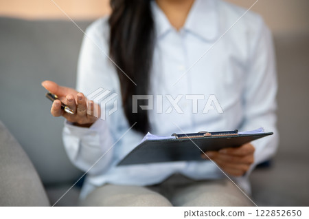 A close-up of a female psychologist holding a medical clipboard and a pen while talking to a patient A close-up of a female psychologist holding a medical clipboard and a pen while talking to a patient 122852650
