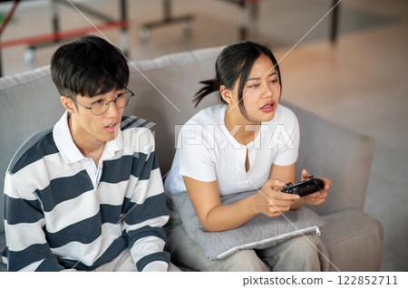 Two young Asian friends are playing a video game together at home. 122852711