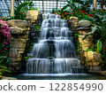 Cascading Waterfall Surrounded by Lush Green Foliage and Vibrant Flowers 122854990
