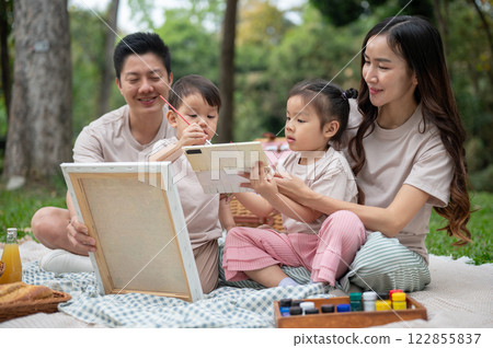 Lovely Asian parents take their little kids on a picnic, enjoying painting on a canvas together. 122855837