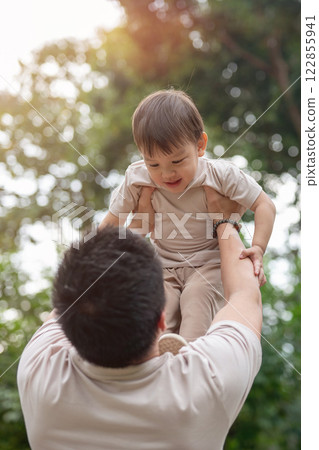 An innocent little Asian boy smiles as his dad lifts him into the air, enjoying a fun time together. An innocent little Asian boy smiles as his dad lifts him into the air, enjoying a fun time together. 122855941