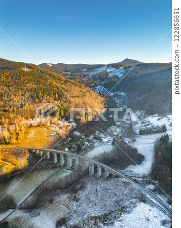 The railway stone bridge in Novina spans across a serene valley, illuminated by the warm hues of a winter sunset. The railway stone bridge in Novina spans across a serene valley, illuminated by the warm hues of a winter sunset. 122856651