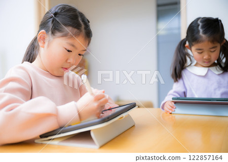 In the backlight, mothers and cram school teachers watch their children studying and doing their homework; smiling elementary school children: "Studying on a tablet is fun" In the backlight, mothers and cram school teachers watch their children studying and doing their homework; smiling elementary school children: "Studying on a tablet is fun" 122857164