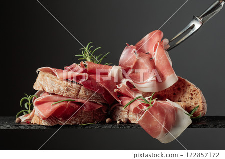 Ciabatta with prosciutto and rosemary on a black background. 122857172