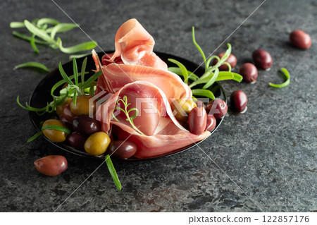 Italian prosciutto crudo with olives and rosemary on a black stone table. 122857176