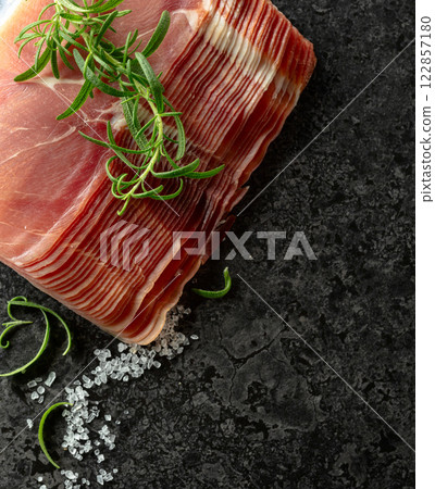 Sliced prosciutto and rosemary on a stone table. Sliced prosciutto and rosemary on a stone table. 122857180