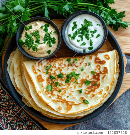 A rustic plate of savory pancakes garnished with fresh parsley, served with two small bowls of cream or yogurt. A rustic plate of savory pancakes garnished with fresh parsley, served with two small bowls of cream or yogurt. 122857328