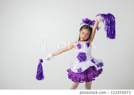 Little cheerleader girl smiling joyfully, dressed in a purple and white outfit. Holding pom-poms in a fun studio image. cheerleader kid 122858973