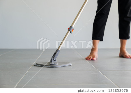 Asian woman mops the floor indoors, cleaning her outdoor front home with a mop and rag. Housewife maintaining a clean home. Represents the concept of professional housekeeping and house cleanup jobs 122858976