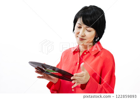 A middle-aged woman in an orange shirt smiling while looking at a record 122859893