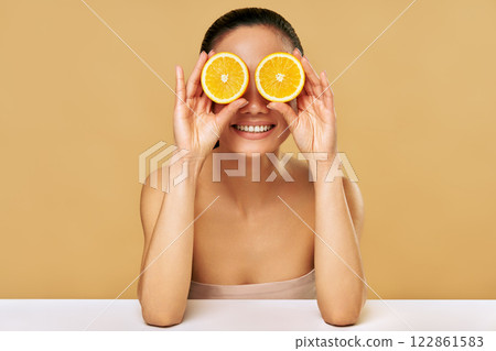 Playful positive asian woman covers eyes with two orange making funny faces Playful positive asian woman covers eyes with two orange making funny faces 122861583