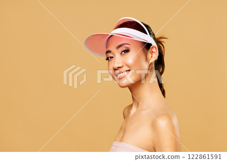 Beautiful asian woman in trendy pink sun visor posing over beige background 122861591