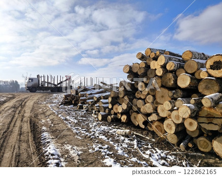 A logging truck on the road and sawn trees stacked in the woods next to the road. winter A logging truck on the road and sawn trees stacked in the woods next to the road. winter 122862165