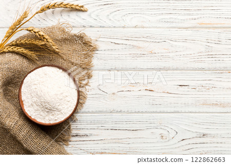 Flat lay of Wheat flour in wooden bowl with wheat spikelets on colored background. world wheat crisis Flat lay of Wheat flour in wooden bowl with wheat spikelets on colored background. world wheat crisis 122862663