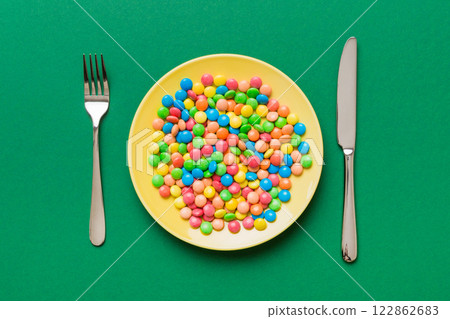 cutlery on table and sweet plate of candy. Health and obesity concept, top view on colored background 122862683