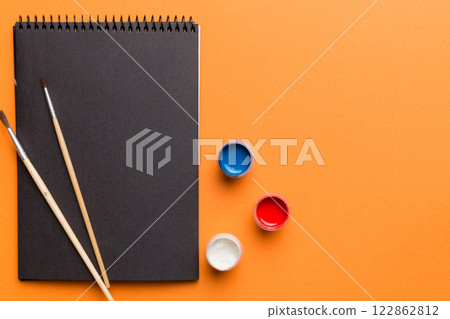 Album pages and paints, pencils, brush on a colored background. Top view with empty space. workplace for creativity. home teaching concept drawing 122862812