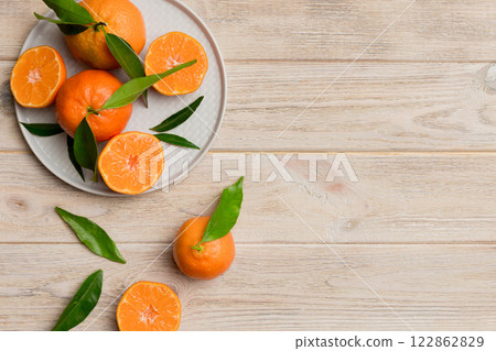 Fresh cutted clementines and whole mandarin over round plate on colored background. Food and drink ingredients preparing. healthy eating theme top view vith copy space 122862829