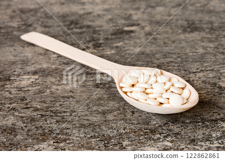 Heap of white pills on colored background. Tablets scattered on a table. Pile of red soft gelatin capsule. Vitamins and dietary supplements concept Heap of white pills on colored background. Tablets scattered on a table. Pile of red soft gelatin capsule. Vitamins and dietary supplements concept 122862861